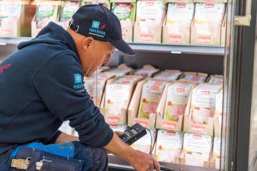 Mitarbeiter prüft und wartet ein Kühlmöbelstück im Supermarkt